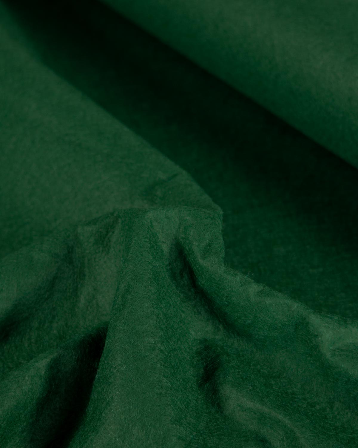 A close-up of dark forest green textured wool and viscose felt fabric with soft folds and a rolled corner, filling the entire frame.