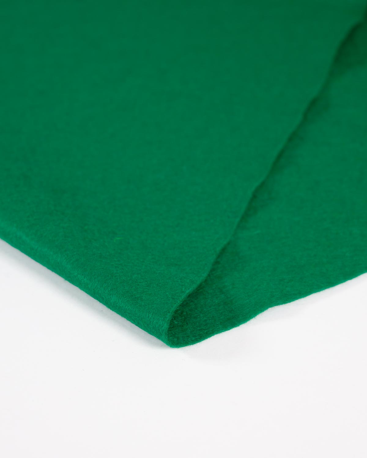 A close-up of jade green wool and viscose felt fabric folded up on a flat white surface showing its even matte surface.