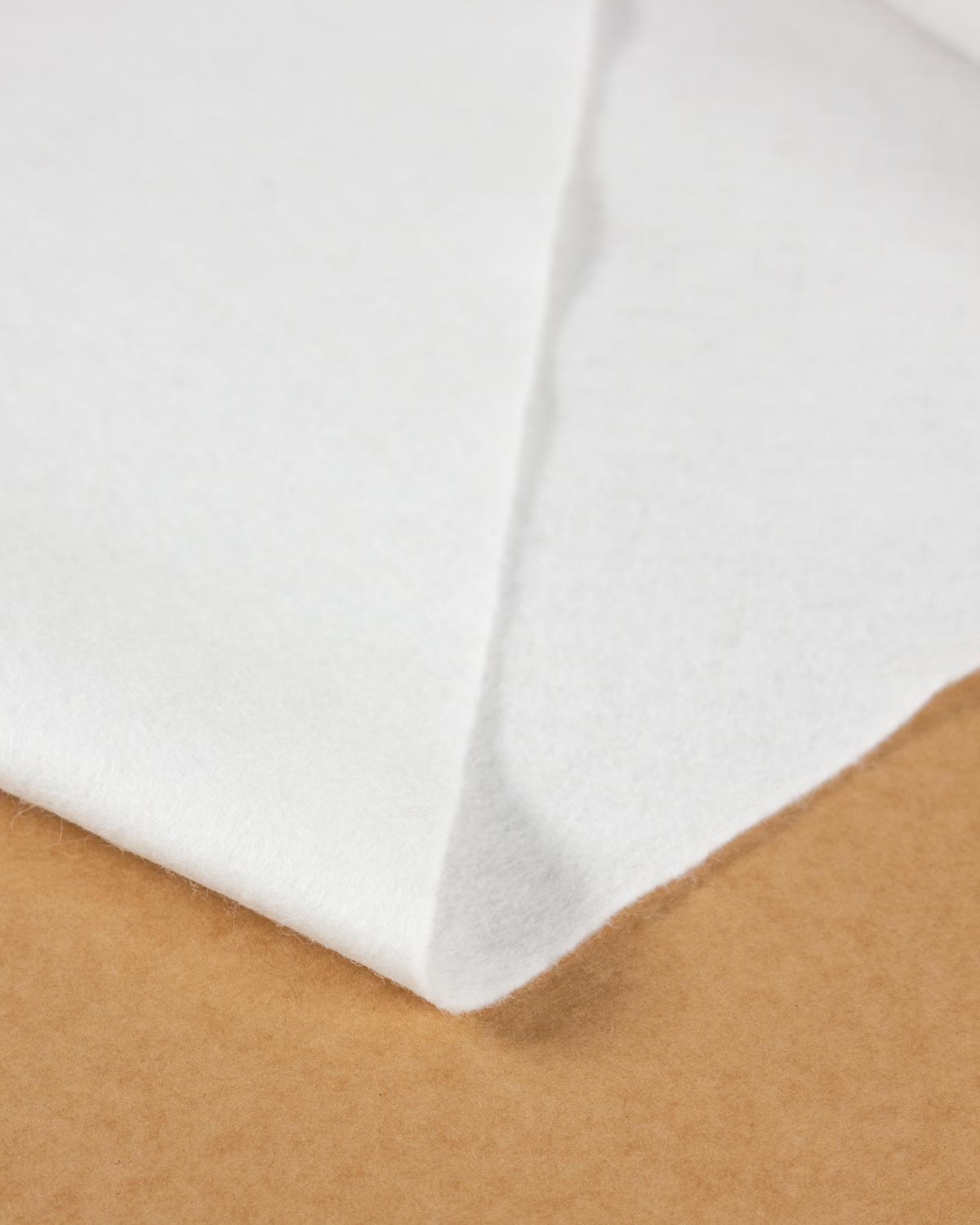 A close-up of a folded bright white wool and viscose felt resting on a brown textured surface, showing its texture and light colour. 