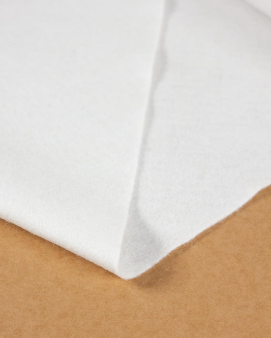 A close-up of a folded bright white wool and viscose felt resting on a brown textured surface, showing its texture and light colour. 