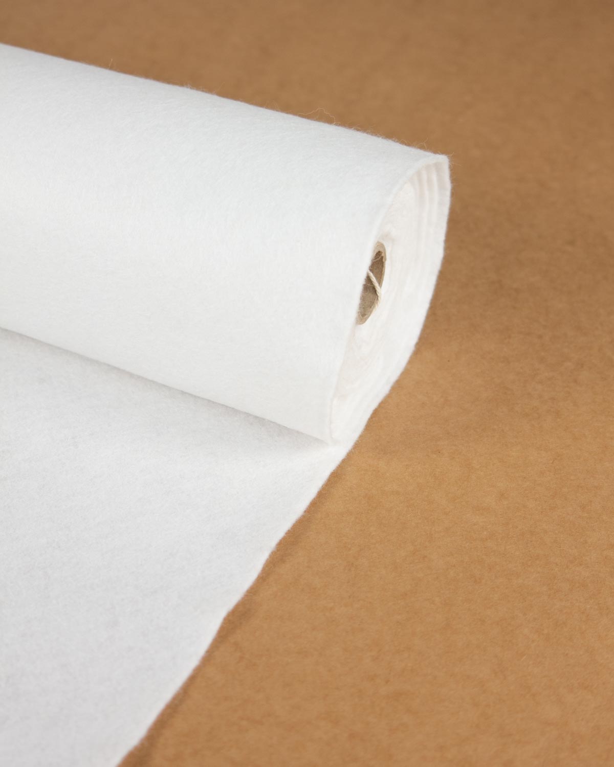 A close-up of a rolled white wool and viscose fabric sheet partially unrolled over a brown textured background.