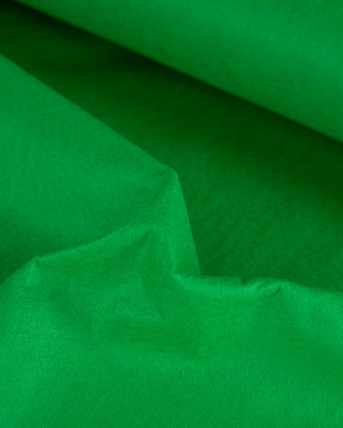 A close-up of bright emerald green wool and viscose felt fabric scrunched up into soft folds showing a slightly textured surface.