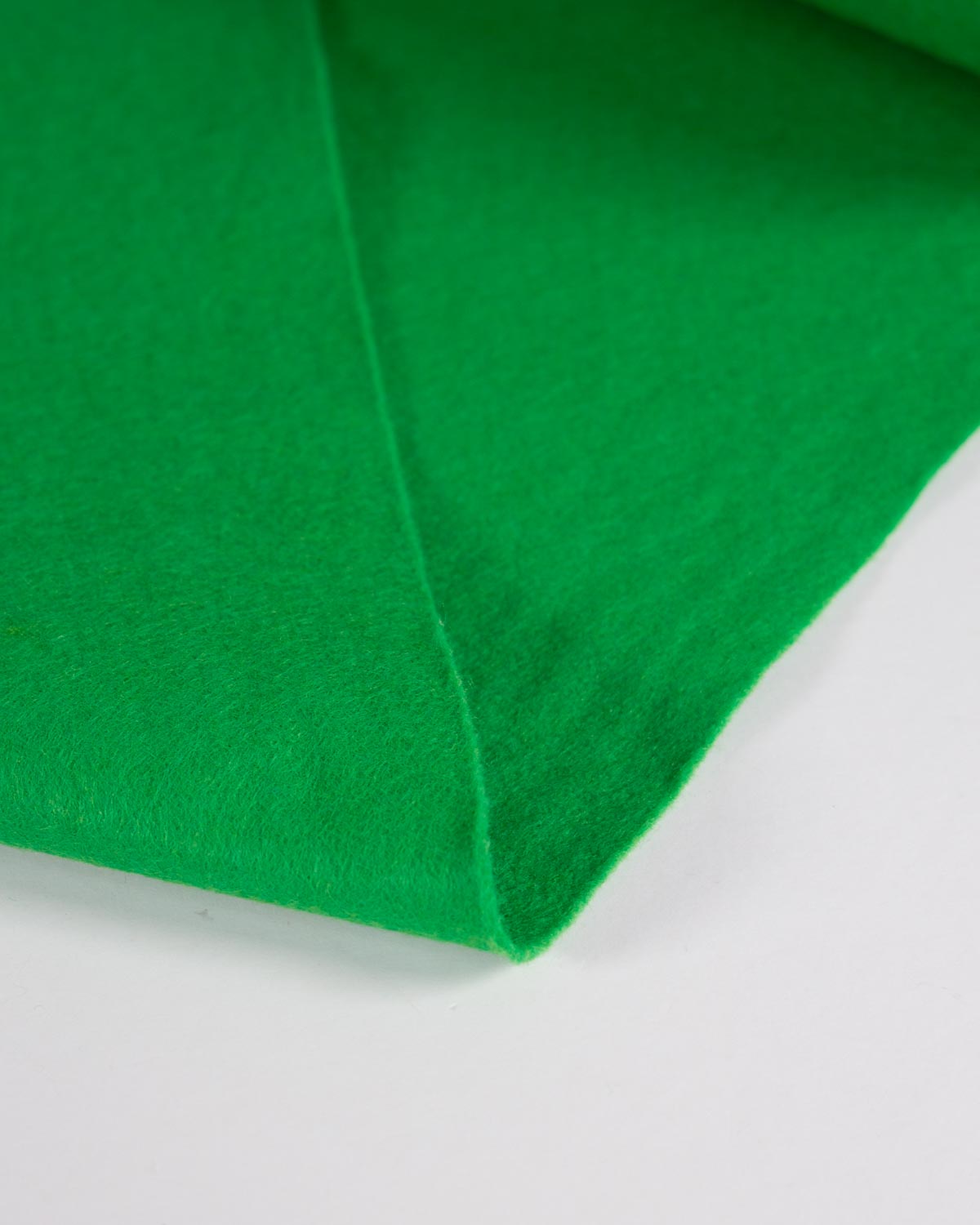 A close-up of bright emerald green wool and viscose felt fabric with a soft, matte texture, folded diagonally on a plain white surface.