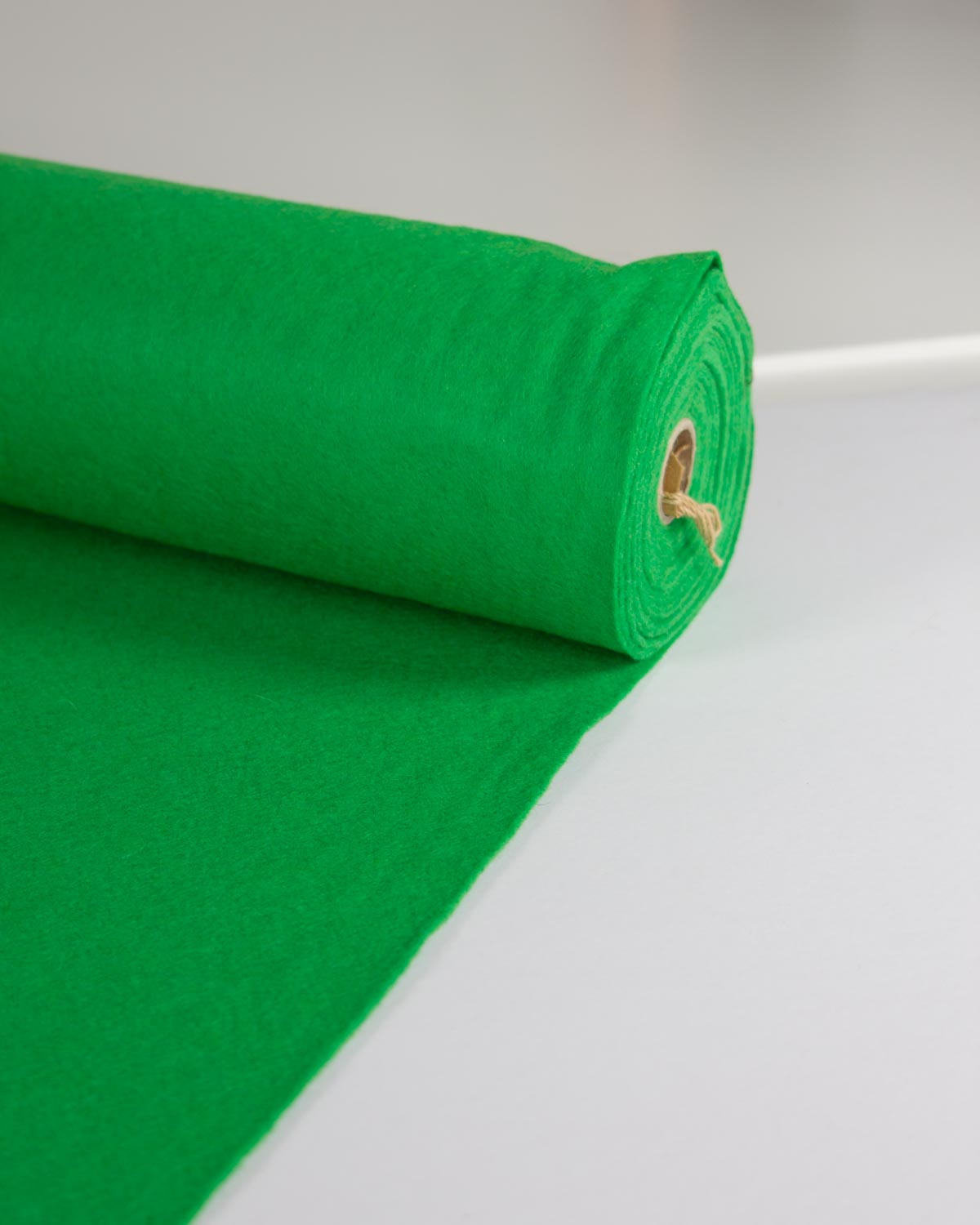 A roll of bright emerald green wool and viscose felt fabric material partially unrolled on a clean white surface.