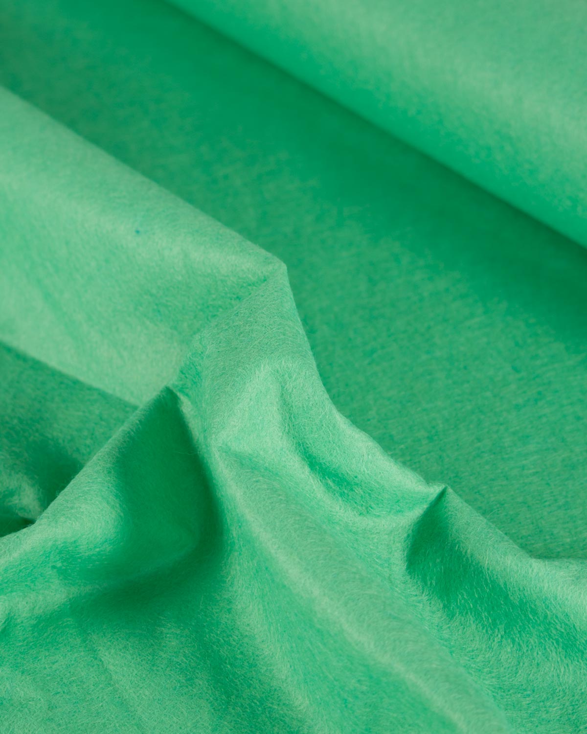 A close-up of draped mint green wool and viscose felt fabric with soft folds and a slightly textured surface.