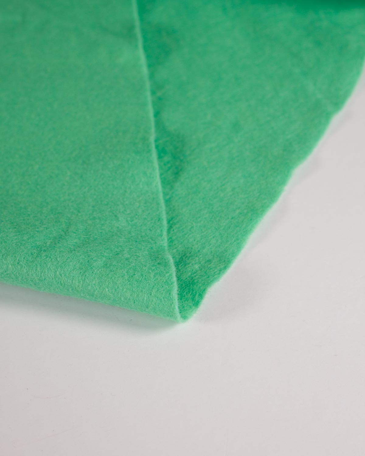 A close-up of bright mint green wool and viscose felt fabric with a soft, matte texture, folded over on a plain white surface.