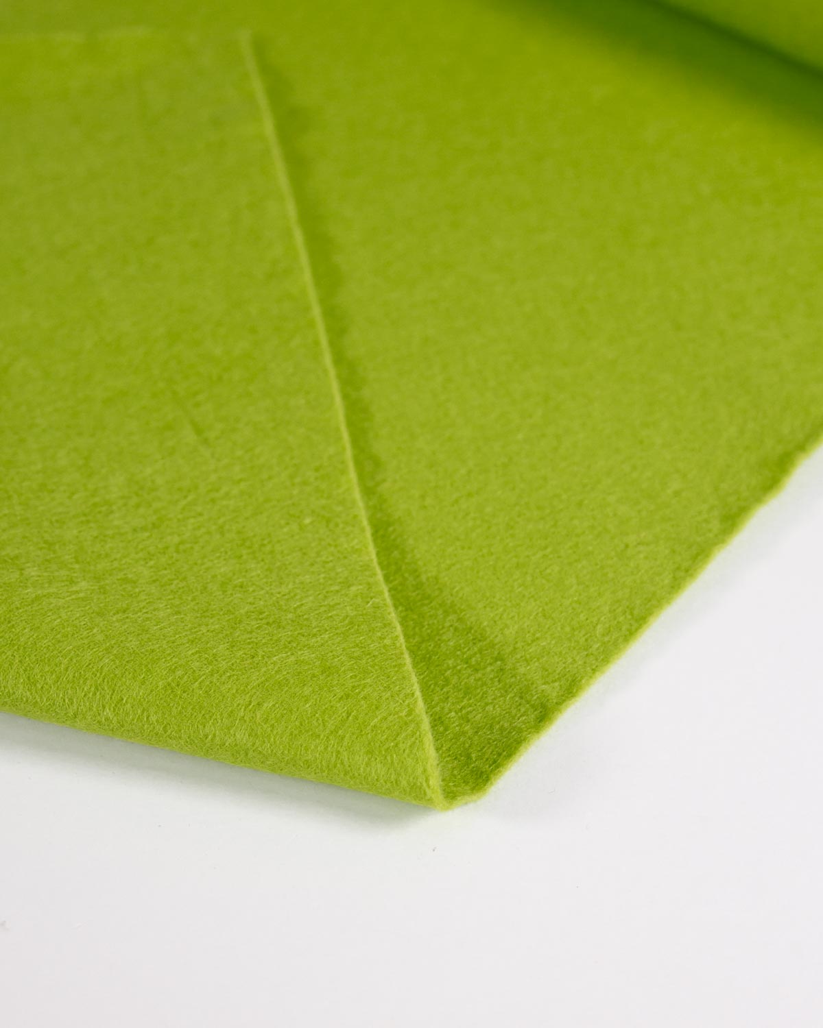 A close-up of bright leaf green wool and viscose felt fabric folded over on a plain white background.