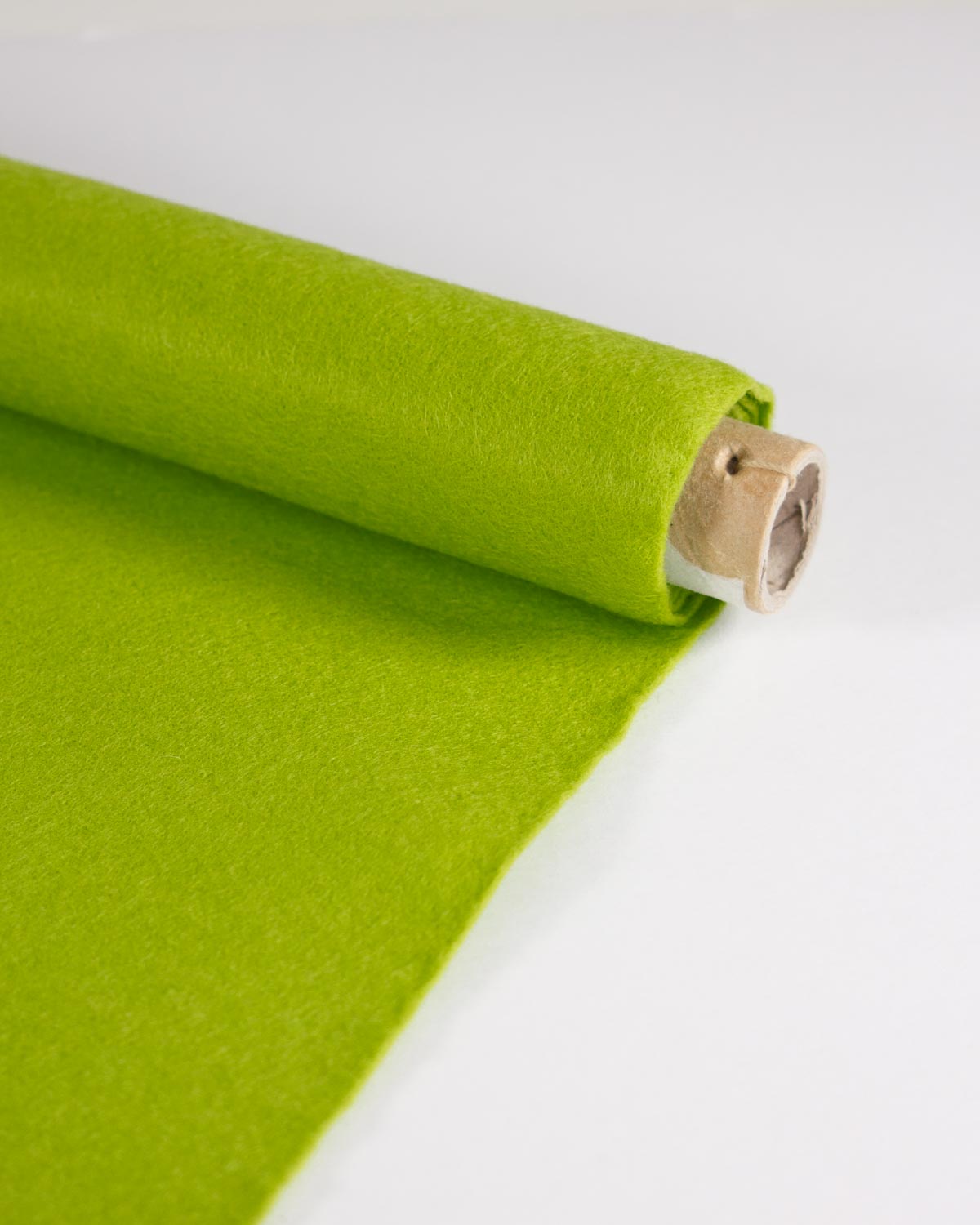 A roll of bright leaf green wool and viscose felt fabric unspooling onto a white surface, showing its soft, matte texture.