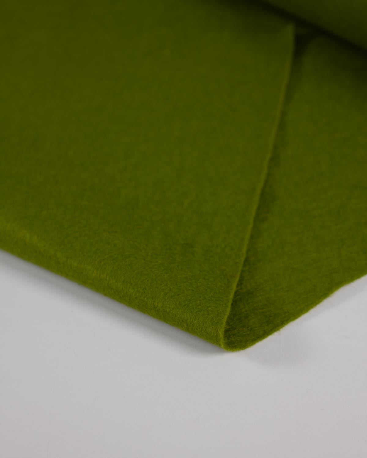 A close-up of a moss green wool and viscose felt fabric folded on a white surface showing its bold, matte texture. 