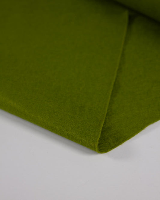 A close-up of a moss green wool and viscose felt fabric folded on a white surface showing its bold, matte texture. 