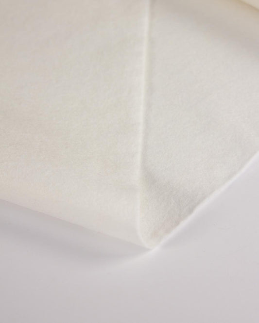 A piece of white natural wool and viscose felt folded on a flat white surface to show its even texture. 