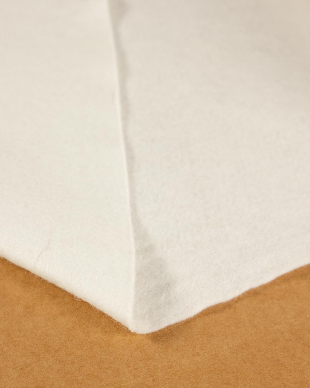 A close-up of a folded off-white natural wool and viscose felt fabric resting on a brown background, showing its even colour and texture. 