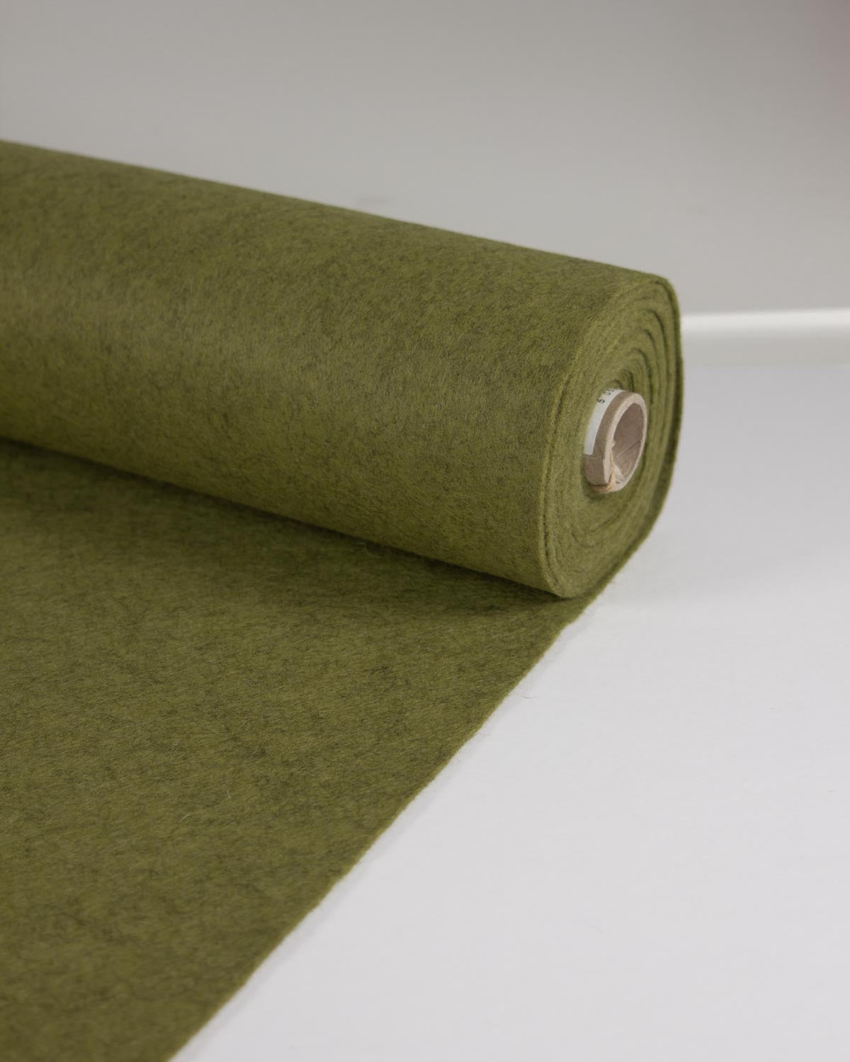 A roll of moss green wool and viscose felt marl fabric unrolled onto a flat white surface. 