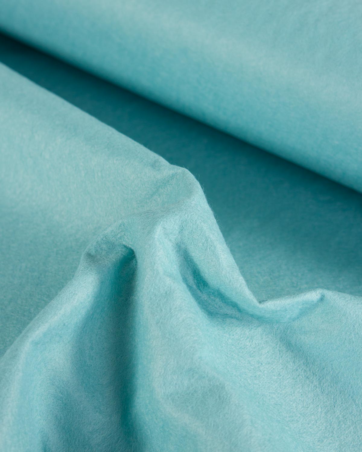 A close-up of draped light turquoise blue wool and viscose felt fabric with a soft, slightly textured surface.