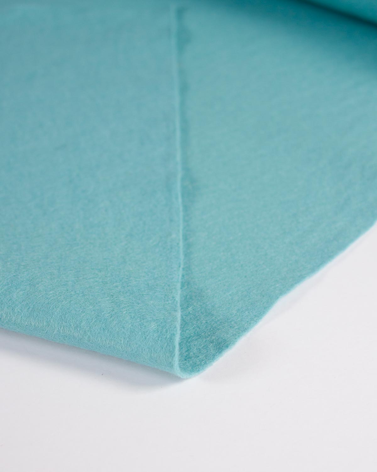 A close-up of a folded piece of light turquoise blue wool and viscose felt fabric on a clean white background.