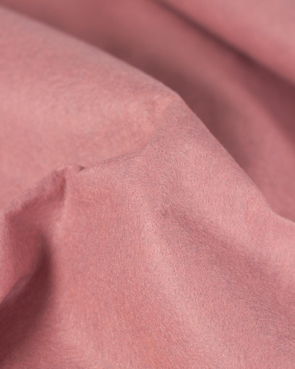 A close-up of draped dusty rose pink wool and viscose felt fabric showing its soft marled texture and folds.