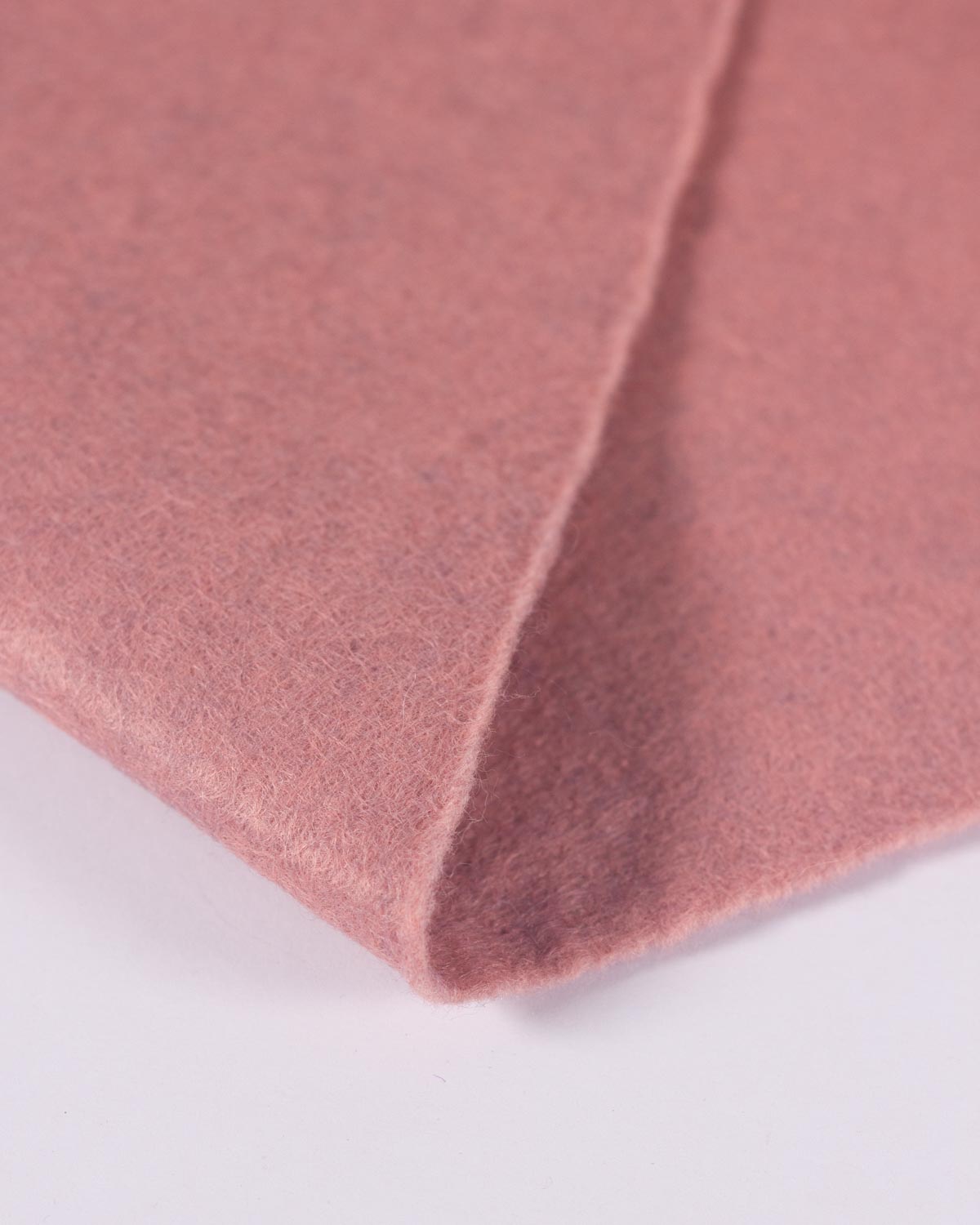 A close-up of a dusty rose pink wool and viscose felt fabric, showing its soft, marled textured surface and folded edges against a clean white background.