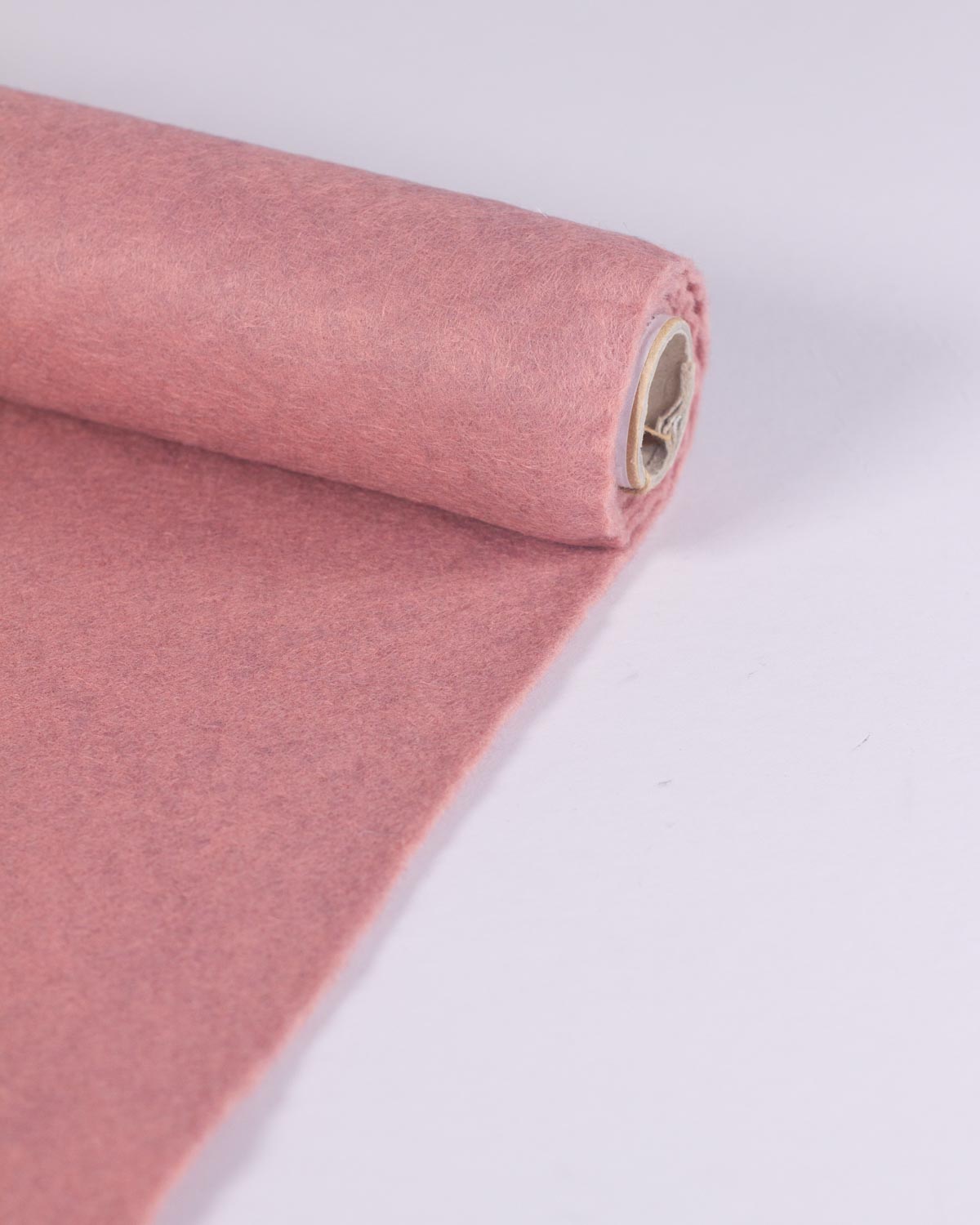 A roll of dusty pink wool and viscose felt fabric, partially unrolled to show its soft, marled textured surface, set against a clean white background.