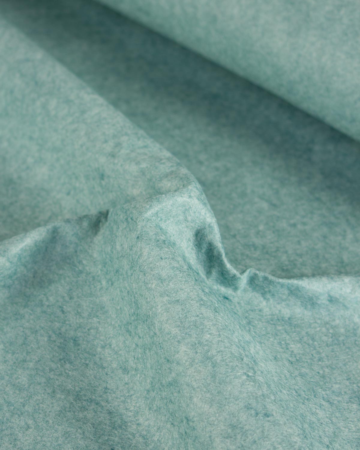 A close-up of draped wool and viscose felt fabric in a muted turquoise blue-green color, showing its soft, textured surface and fine fibrous structure.