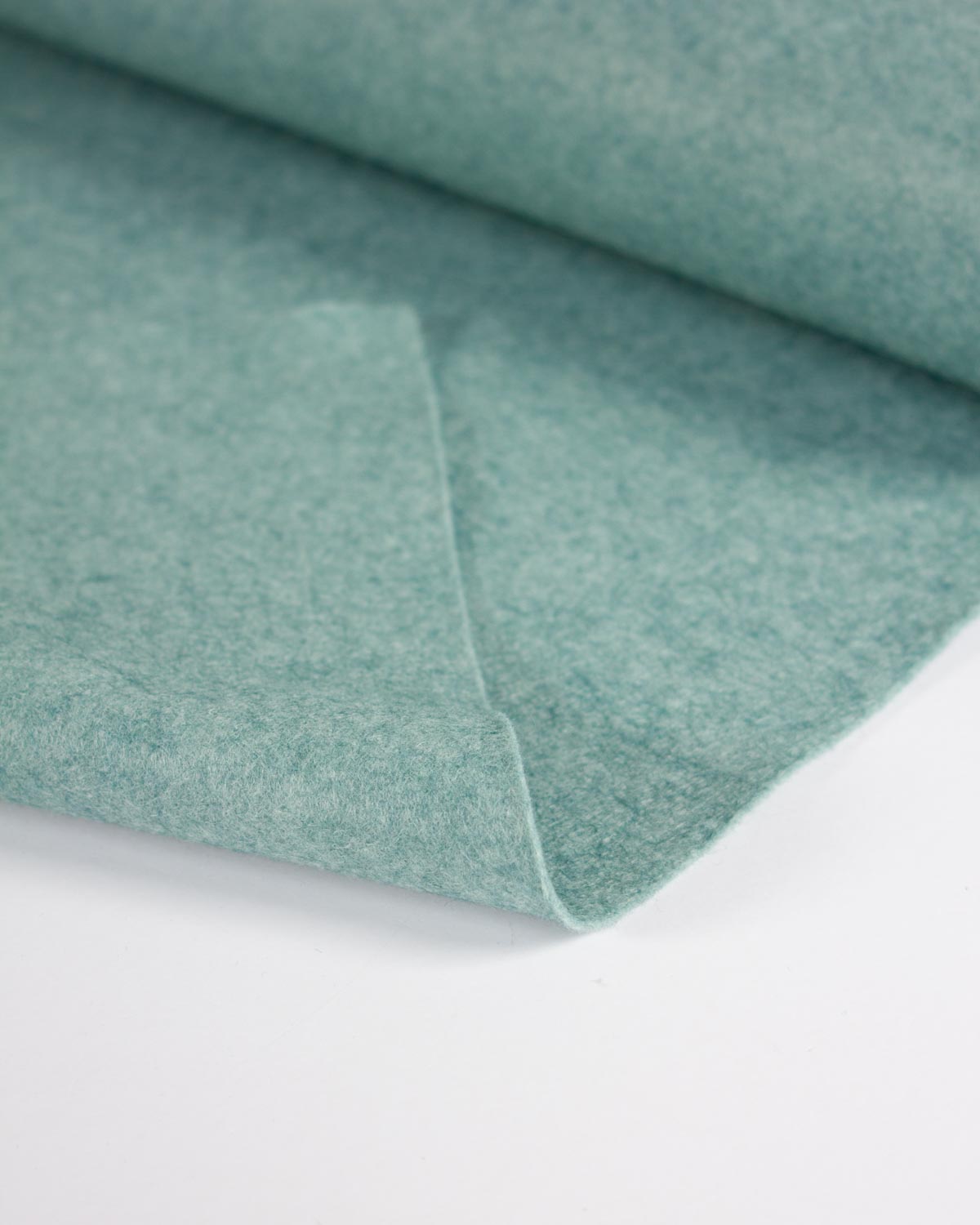 A close-up of a folded piece of turquoise blue-green wool and viscose felt fabric on a clean white background.