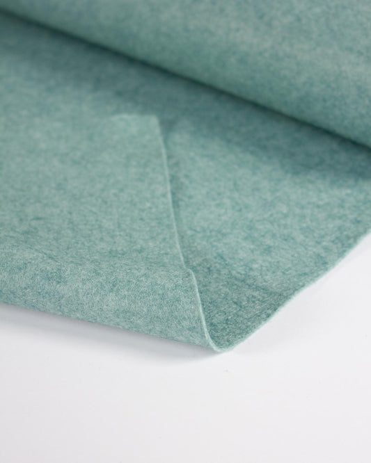 A close-up of a folded piece of turquoise blue-green wool and viscose felt fabric on a clean white background.