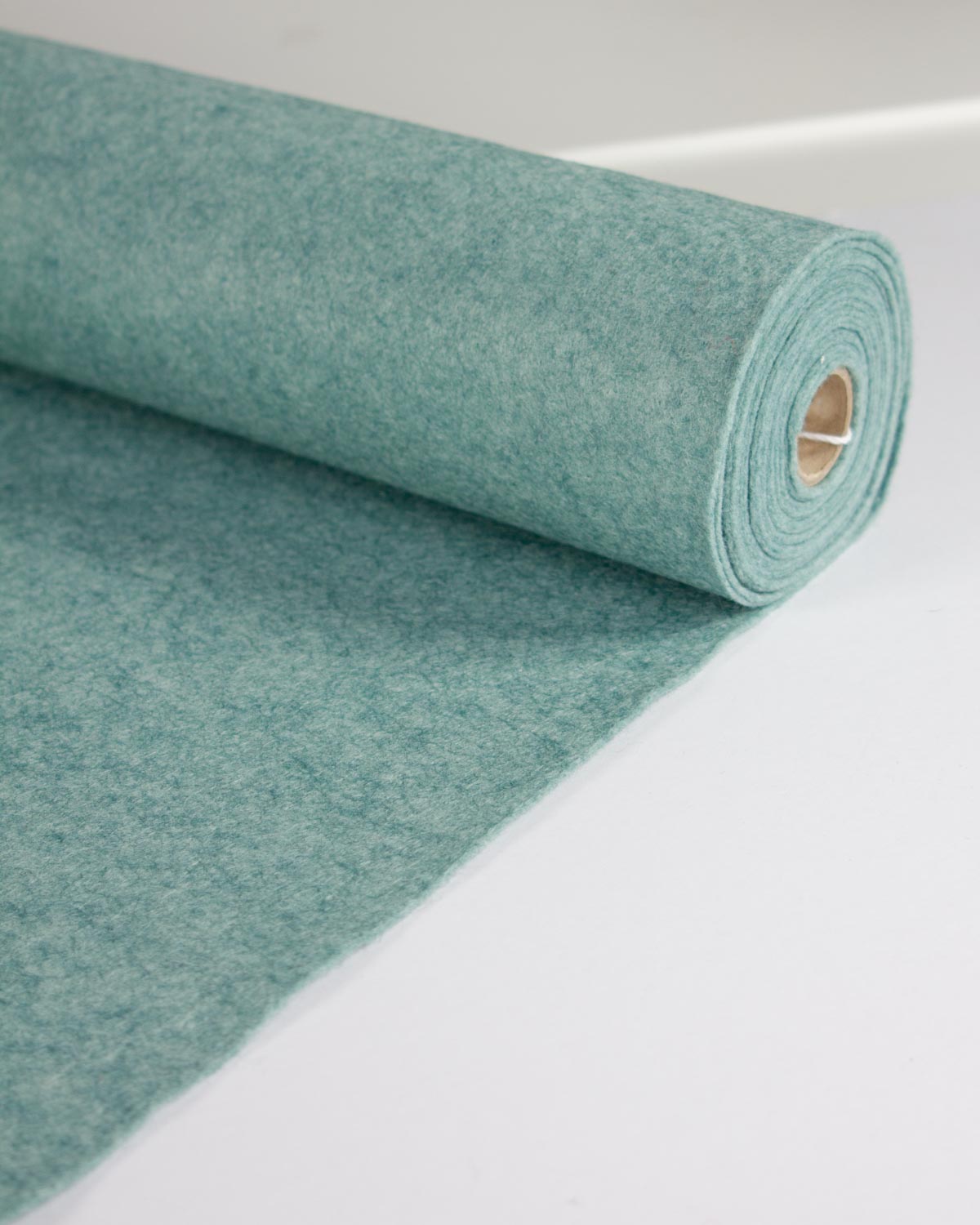 A roll of textured wool and viscose felt fabric in a muted turquoise blue-green color, partially unrolled on a clean white surface.