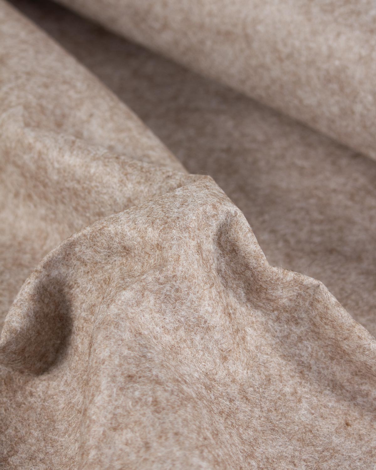 A close-up of draped fawn marl beige wool and viscose felt fabric with a soft, textured surface.