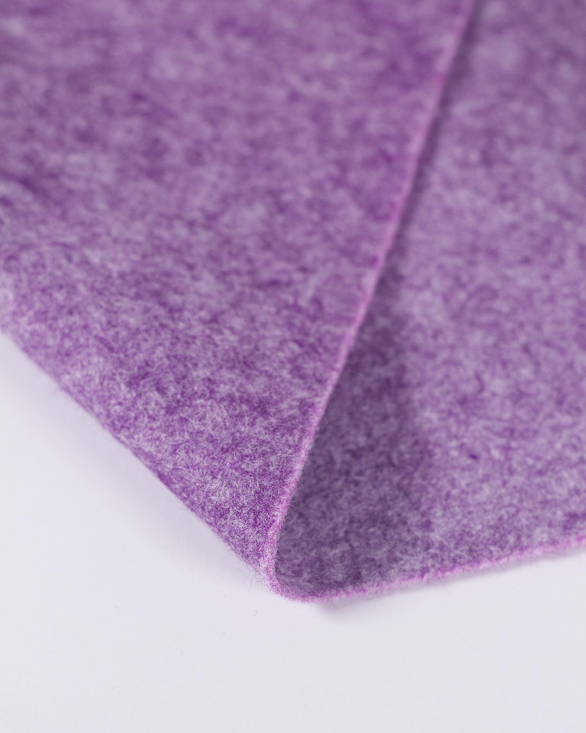 A close-up of a folded purple heather marl piece of wool and viscose felt fabric, showing its textured marled surface and colour on a white plain backdrop. 