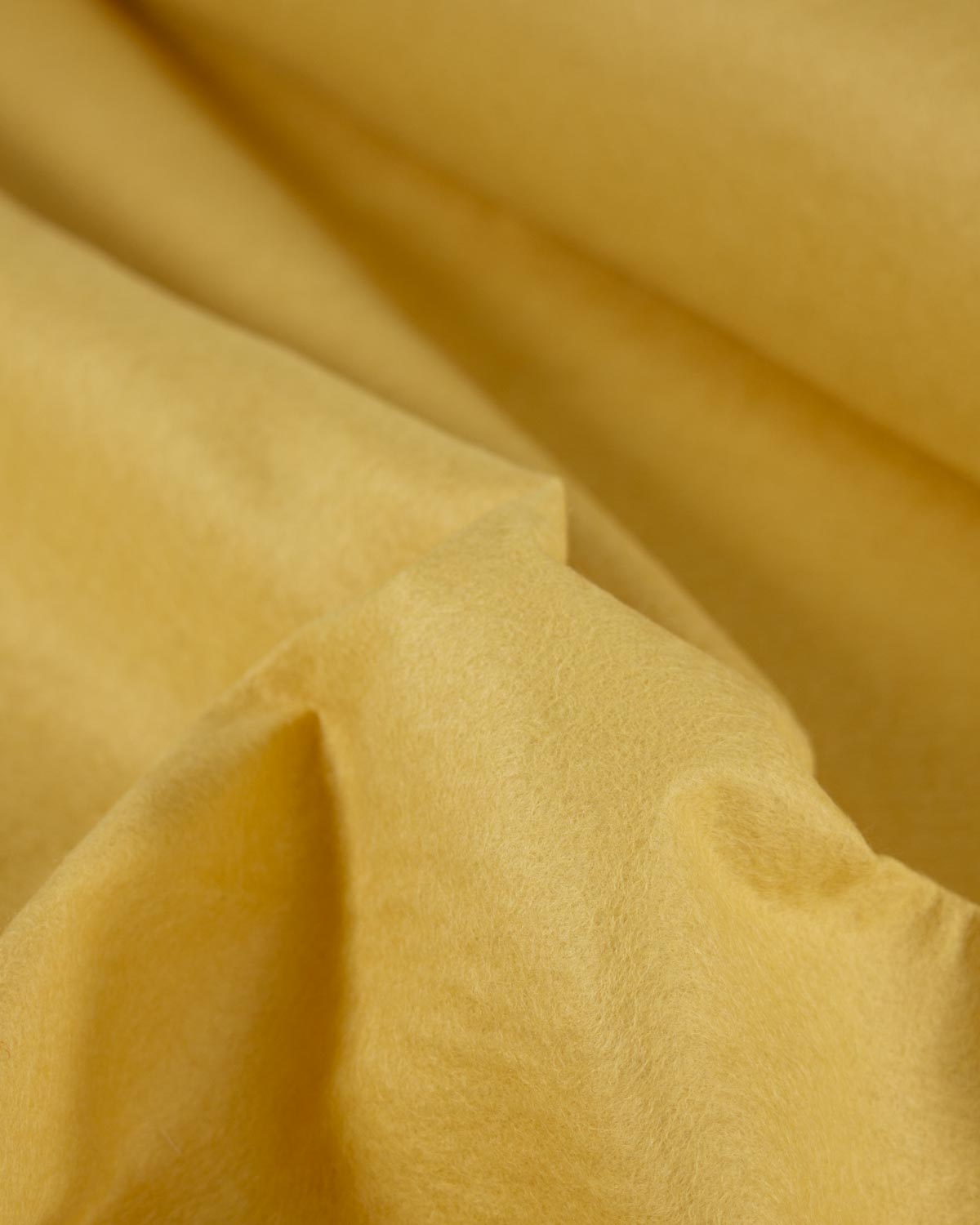 A close-up of draped yellow wool and viscose felt fabric with soft folds and a matte texture.
