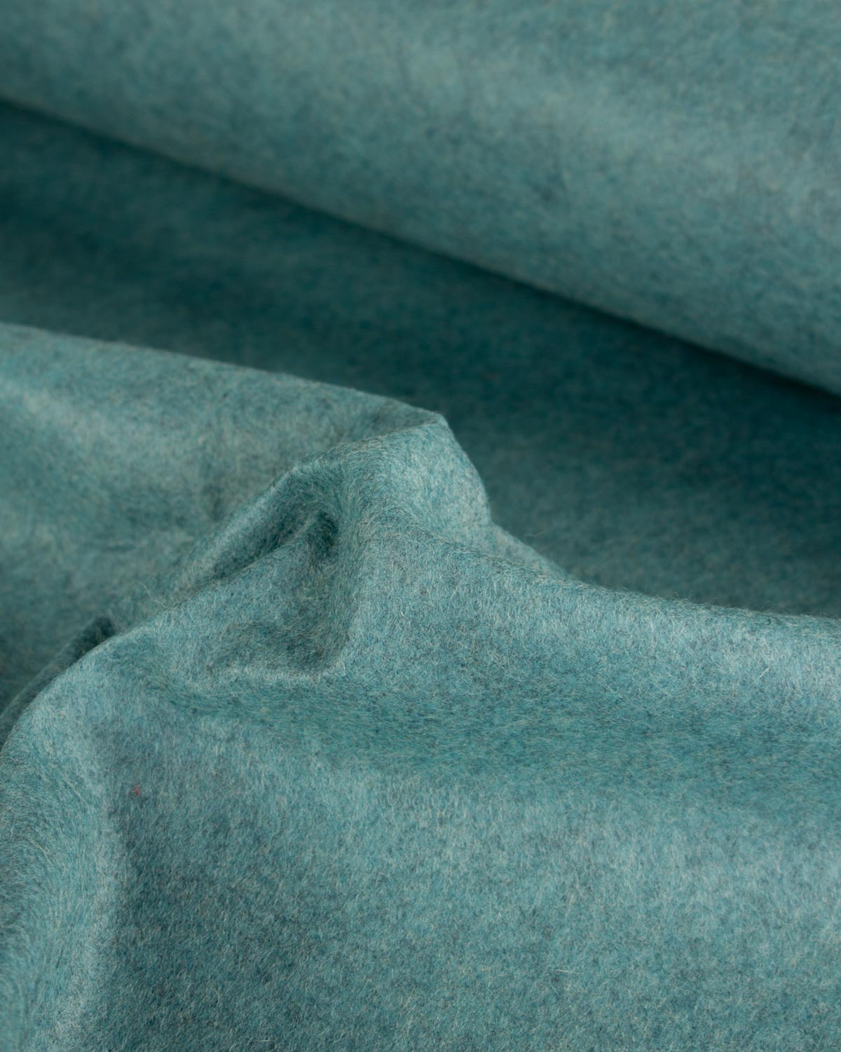A close-up of draped wool and viscose felt fabric in a muted teal-blue jade marl color, showing its soft, textured surface and folds.