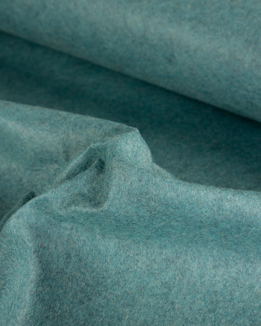 A close-up of draped wool and viscose felt fabric in a muted teal-blue jade marl color, showing its soft, textured surface and folds.