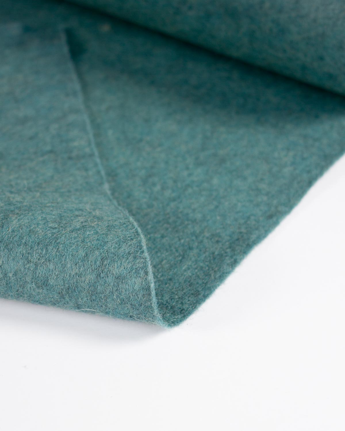 A close-up of a jade blue marl wool and viscose felt fabric folded on a plain white surface. 