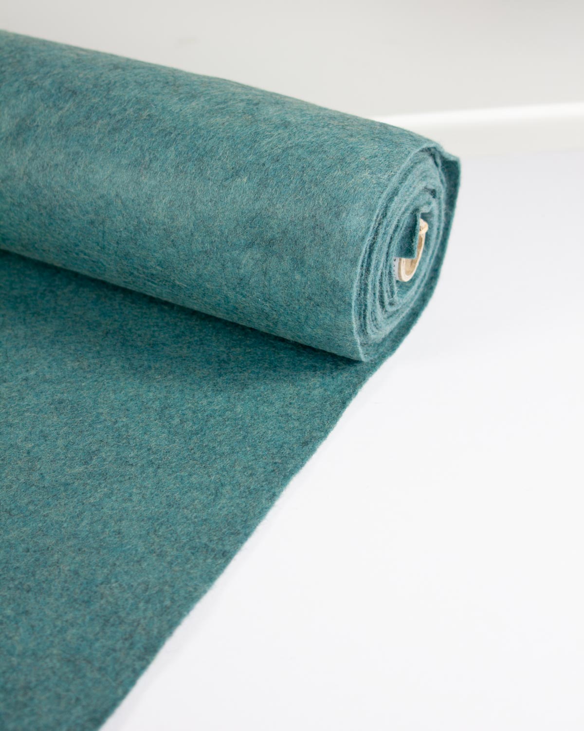 A roll of teal jade marl wool and viscose felt fabric, partially unrolled on a clean white surface.