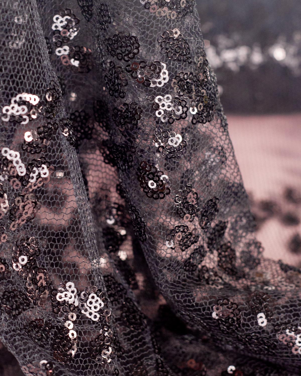 A draped piece of black sequined tulle fabric with small black sequins in a leaf pattern. 