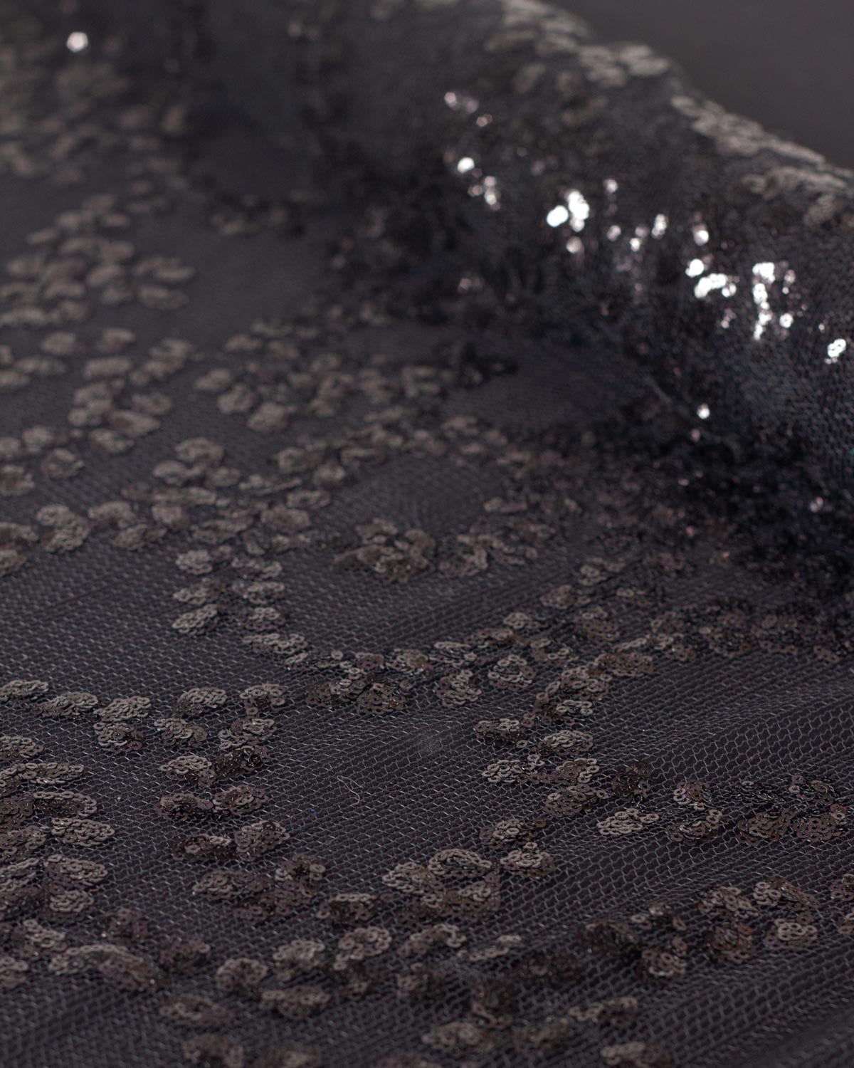 Close-up of black sequined tulle fabric with a floral leaf pattern, showing the shimmering sequins and sheer netting texture.