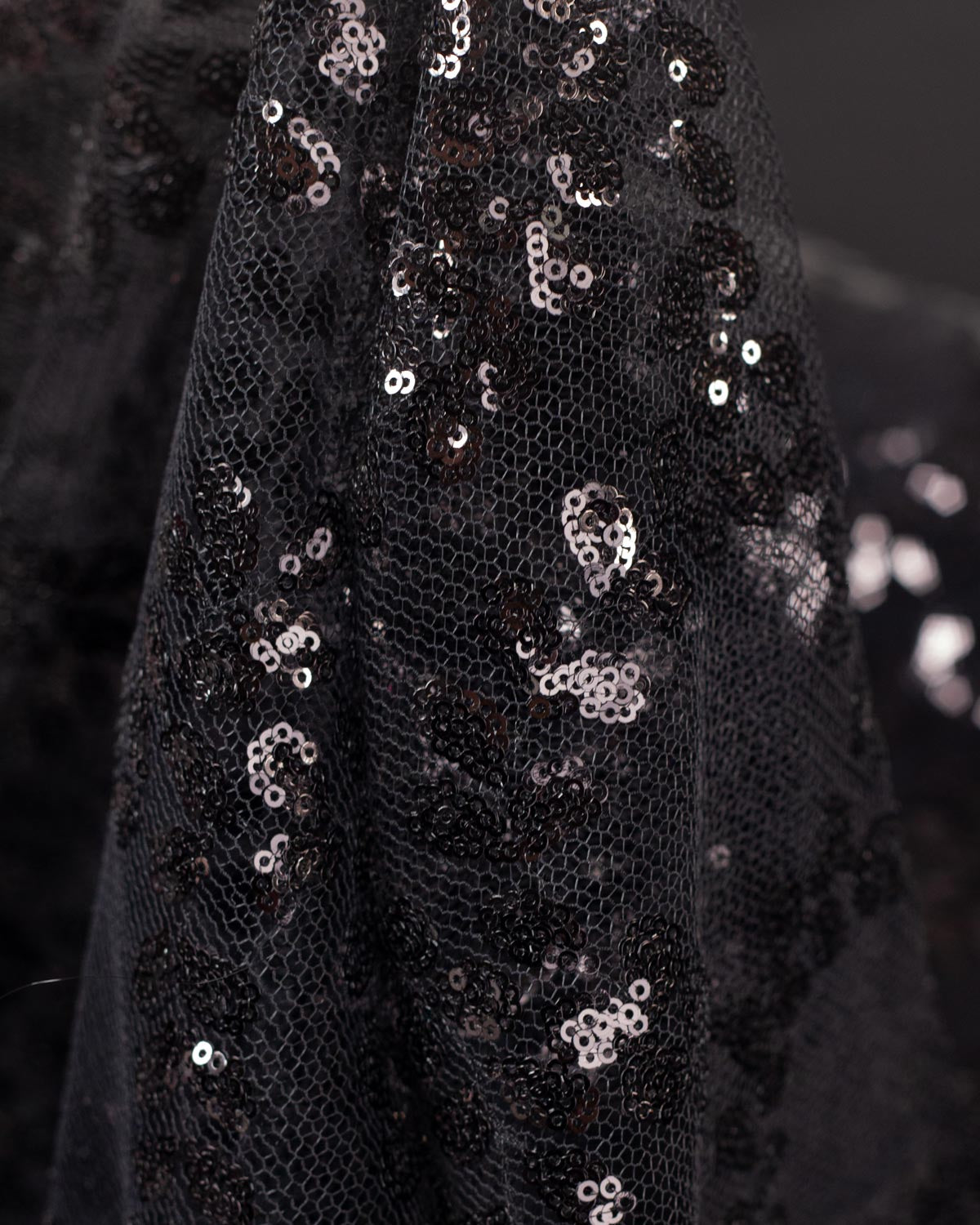 Close-up of draped black sequined tulle fabric with small black sequins arranged in a floral leaf pattern. 