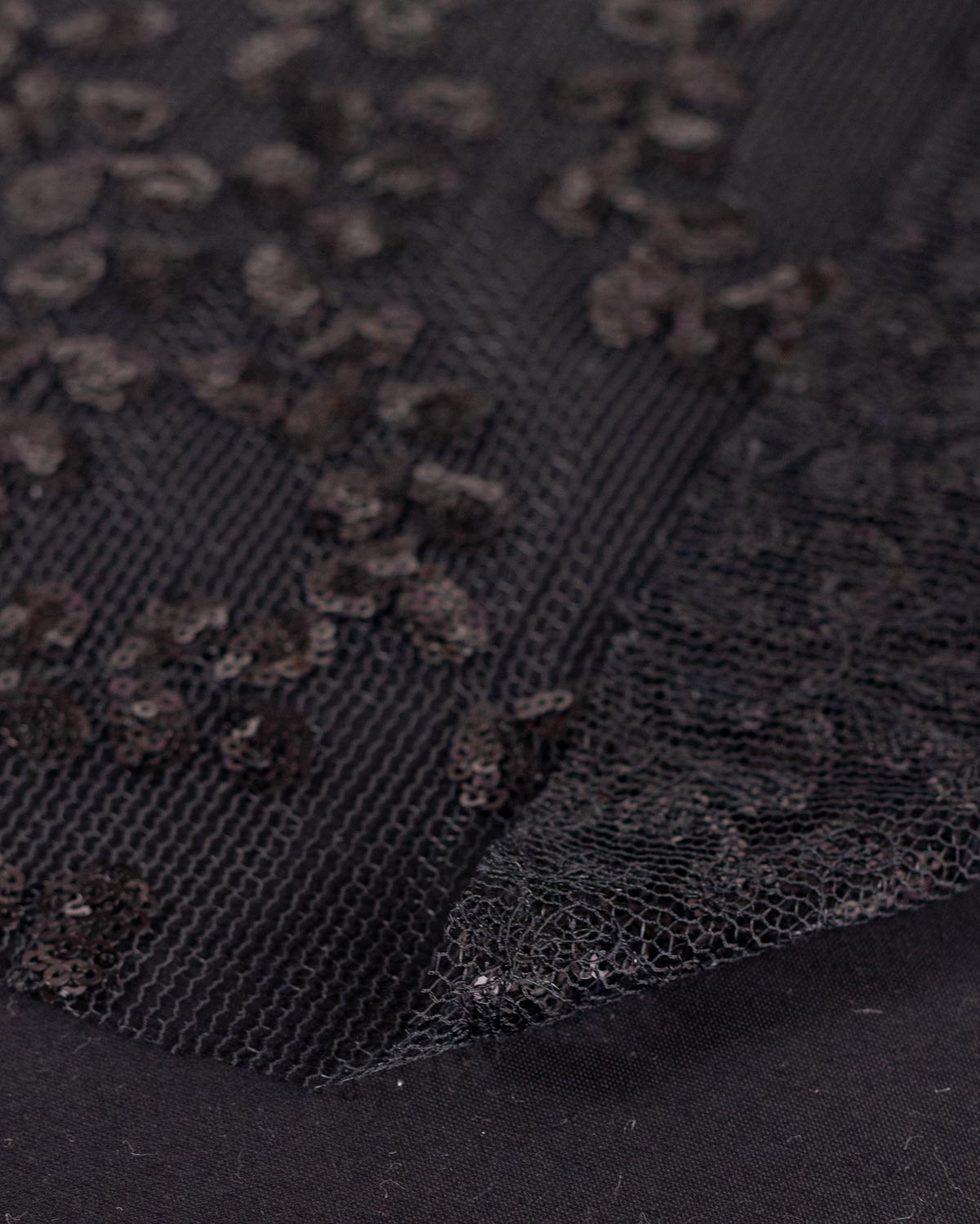 Close-up of black tulle fabric with a floral leaf pattern of black sequins, showing the texture and layered embellishment.