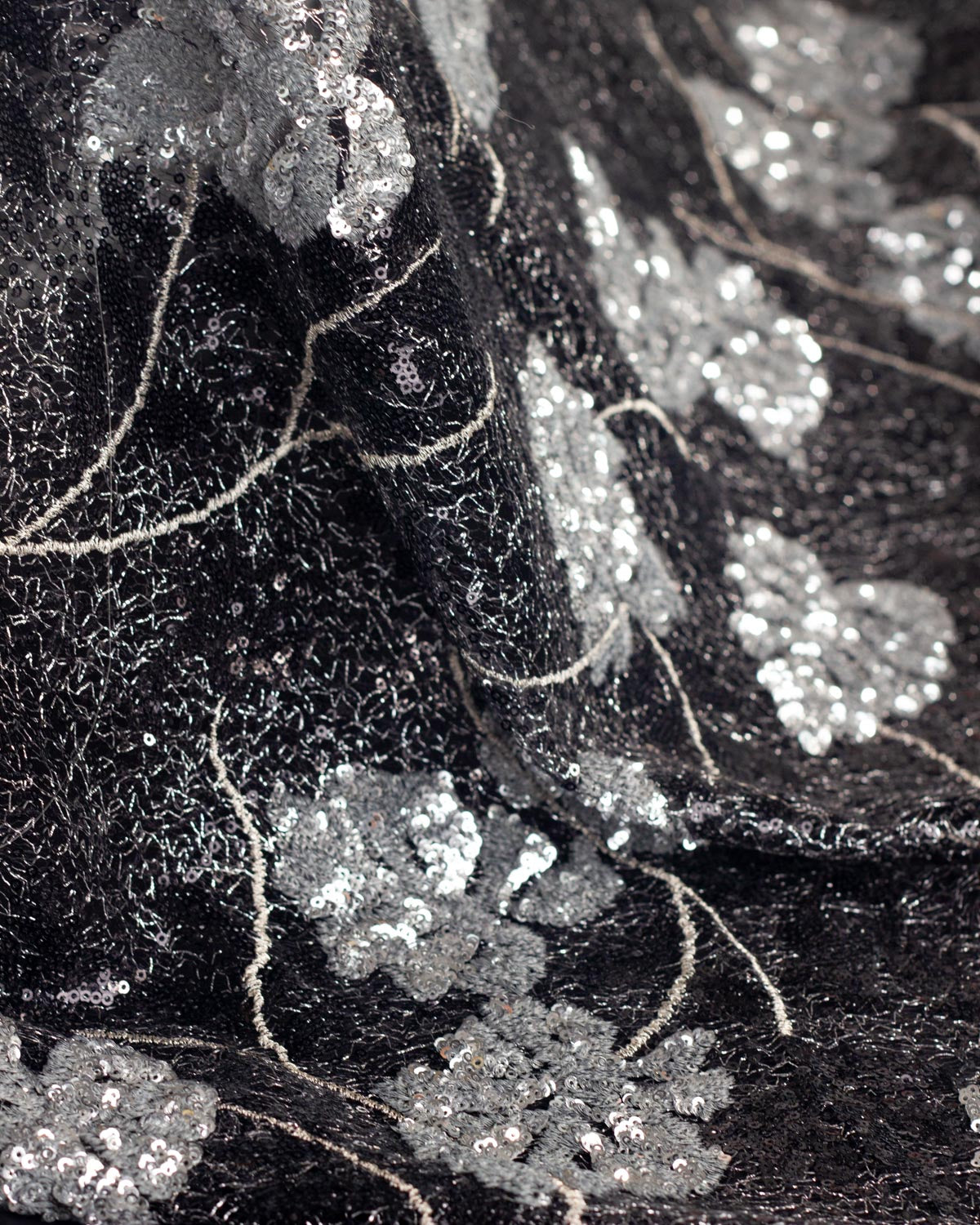 Close-up of draped black sequined cobweb tulle fabric with silver monstera leaf applique and thin silver embroidered stems.