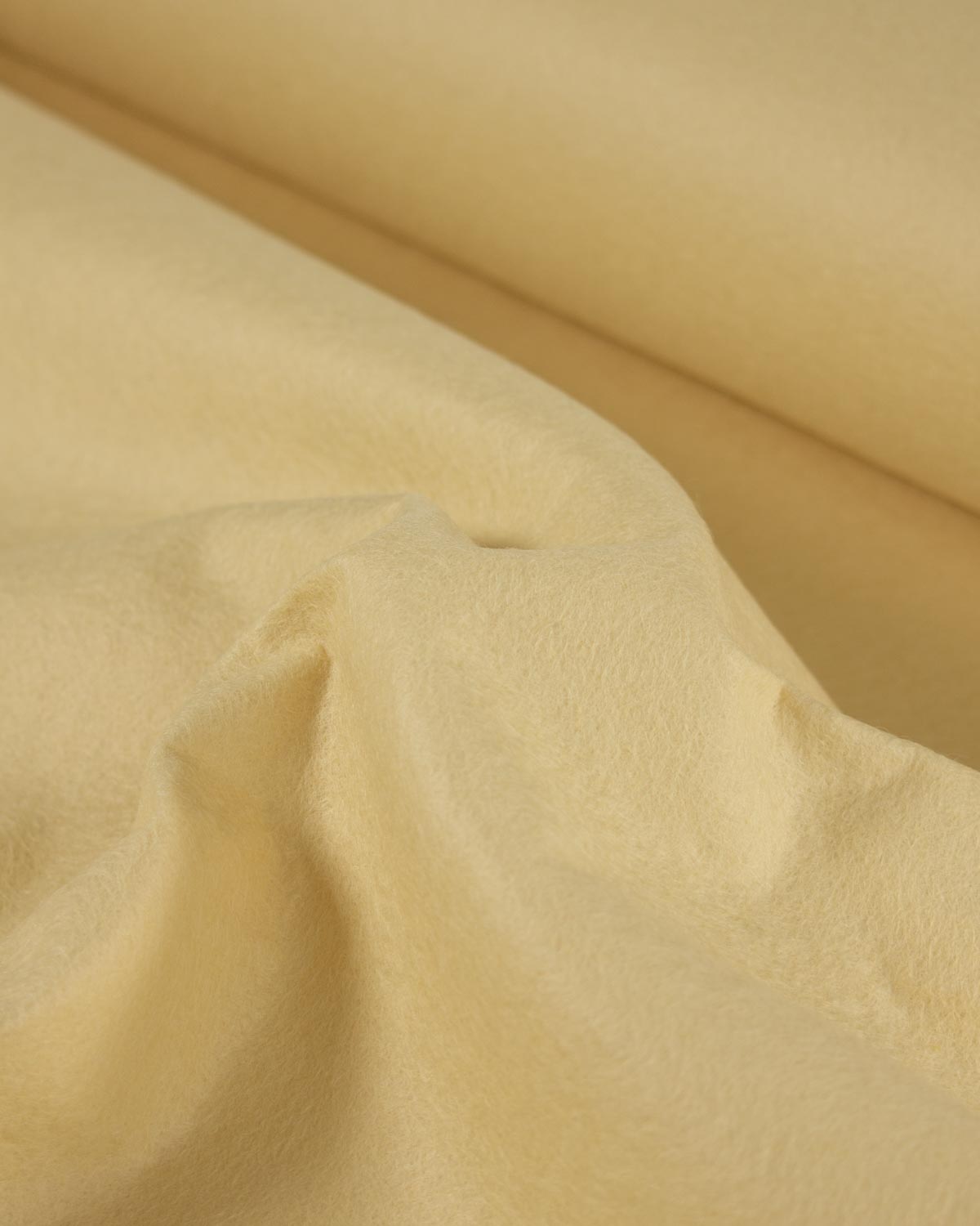A close-up of draped yellow cream-colored fabric with soft folds and a smooth texture.