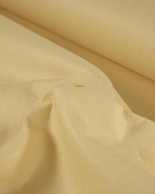 A close-up of draped yellow cream-colored fabric with soft folds and a smooth texture.