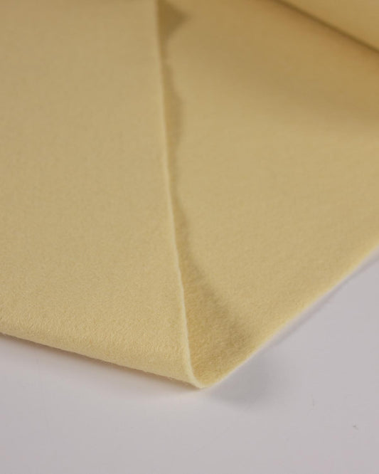 A close-up of a folded piece of yellow cream wool and viscose felt fabric on a white background.