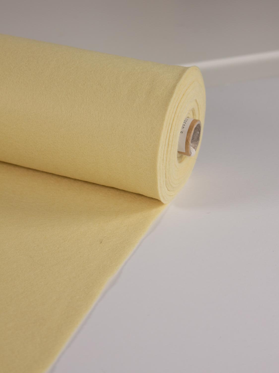 A roll of pale yellow cream wool and viscose felt fabric partially unrolled on a clean white surface.