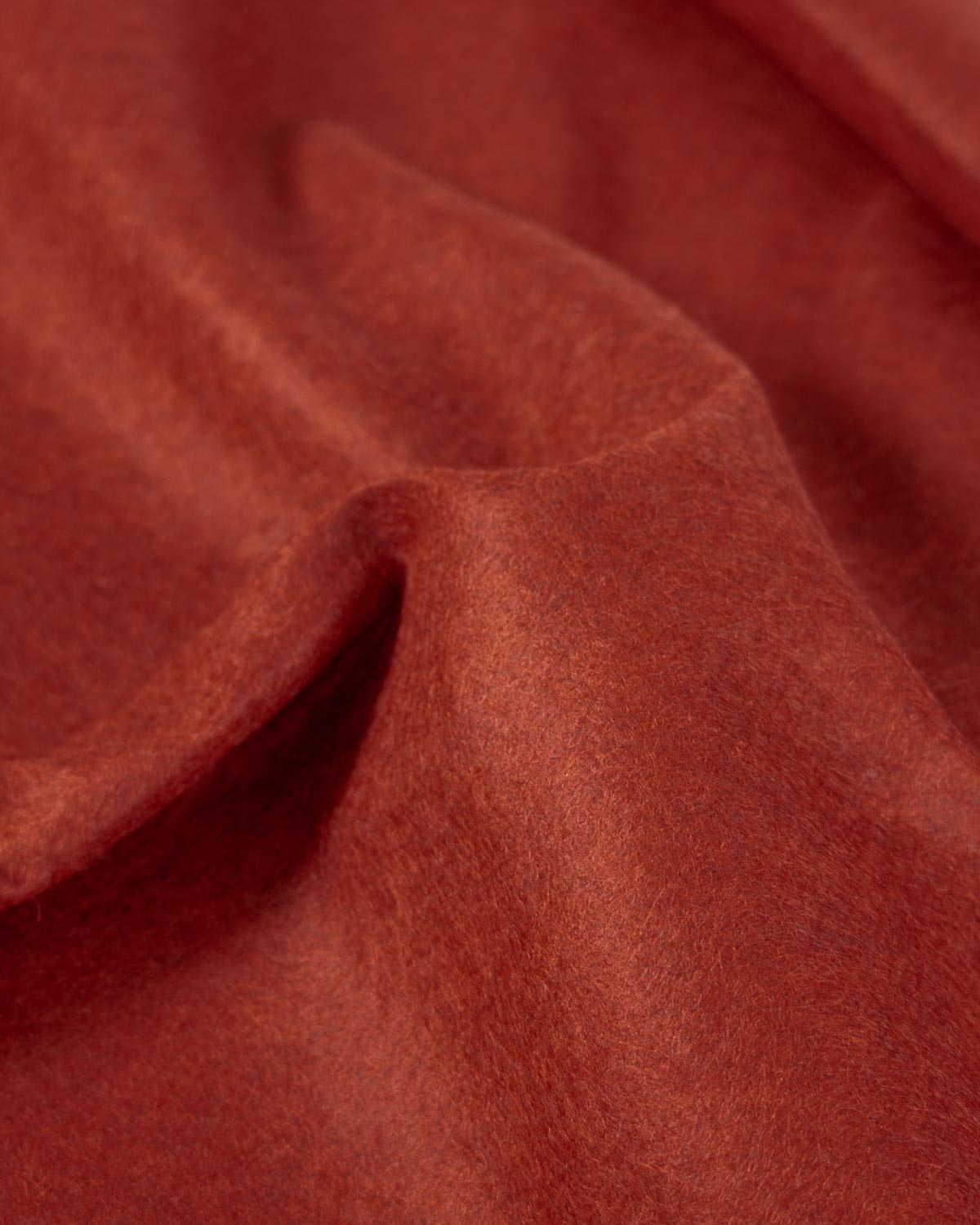 A gathered piece of terracotta red/orange wool and viscose felt fabric, showing its marled texture and firm structure. 
