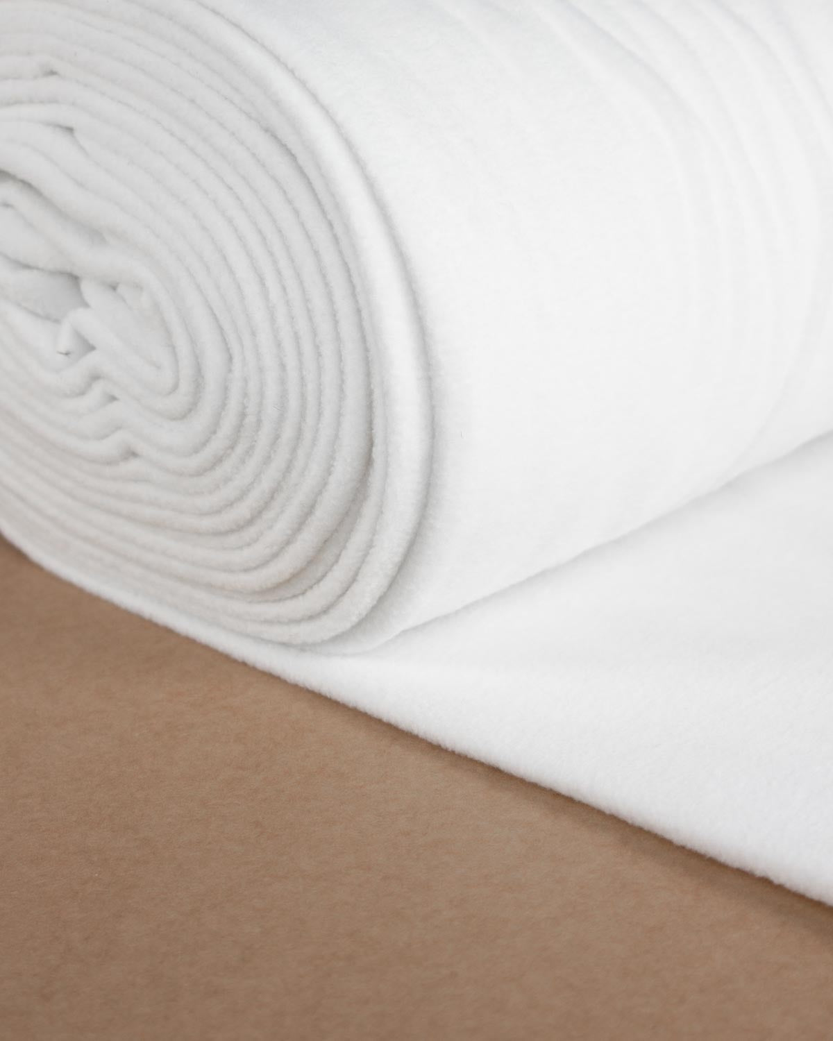 A close-up of a rolled white, plush fleece fabric resting on a plain brown surface.