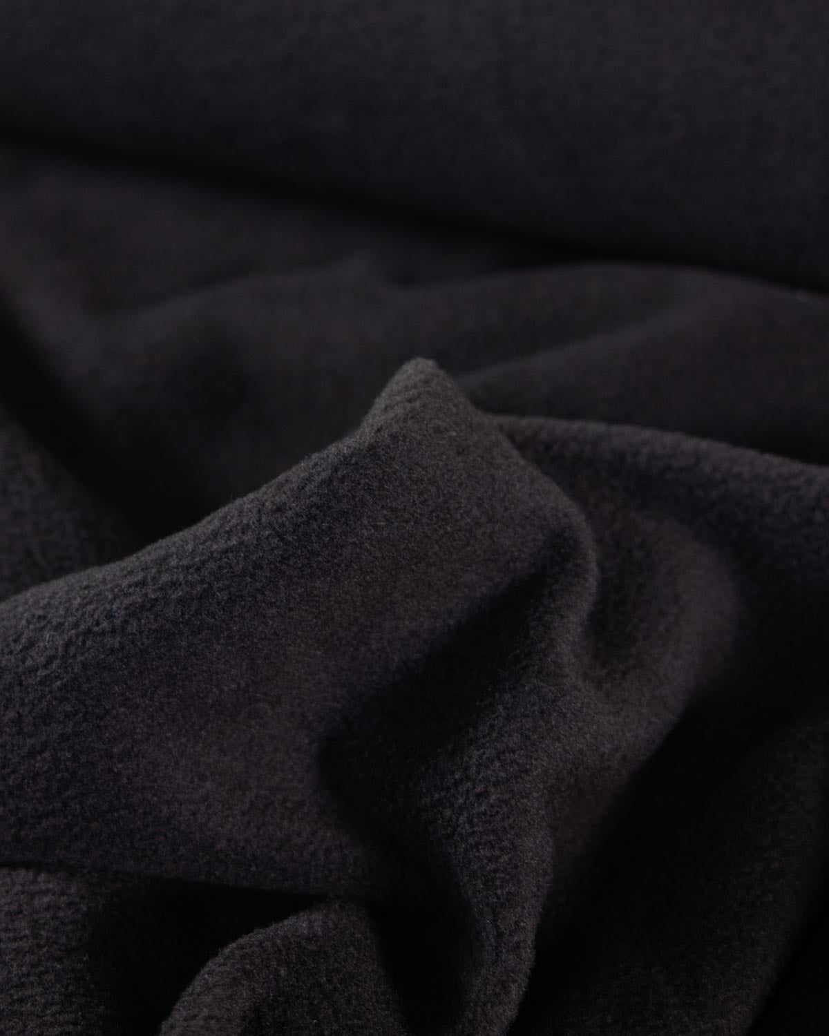 A close-up of black textured fleece fabric, showing a soft, plush surface with folds and shadows.