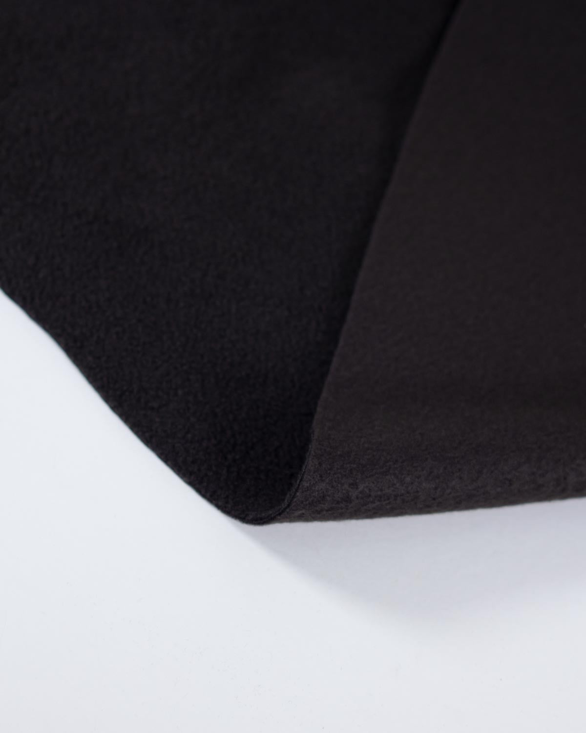 A close-up of a black textured fleece fabric, showing its soft, fuzzy pile on one side and a smoother matte reverse on the folded over side, set against a clean white background.