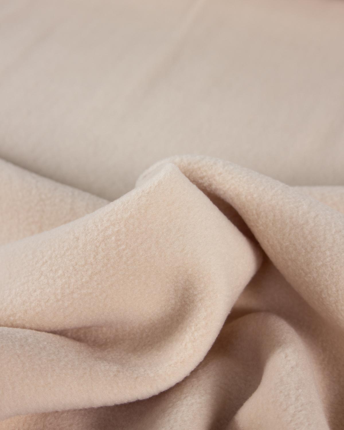 A close-up of soft, plush fleece fabric in a light warm beige or cream color, shown with gentle folds and texture.