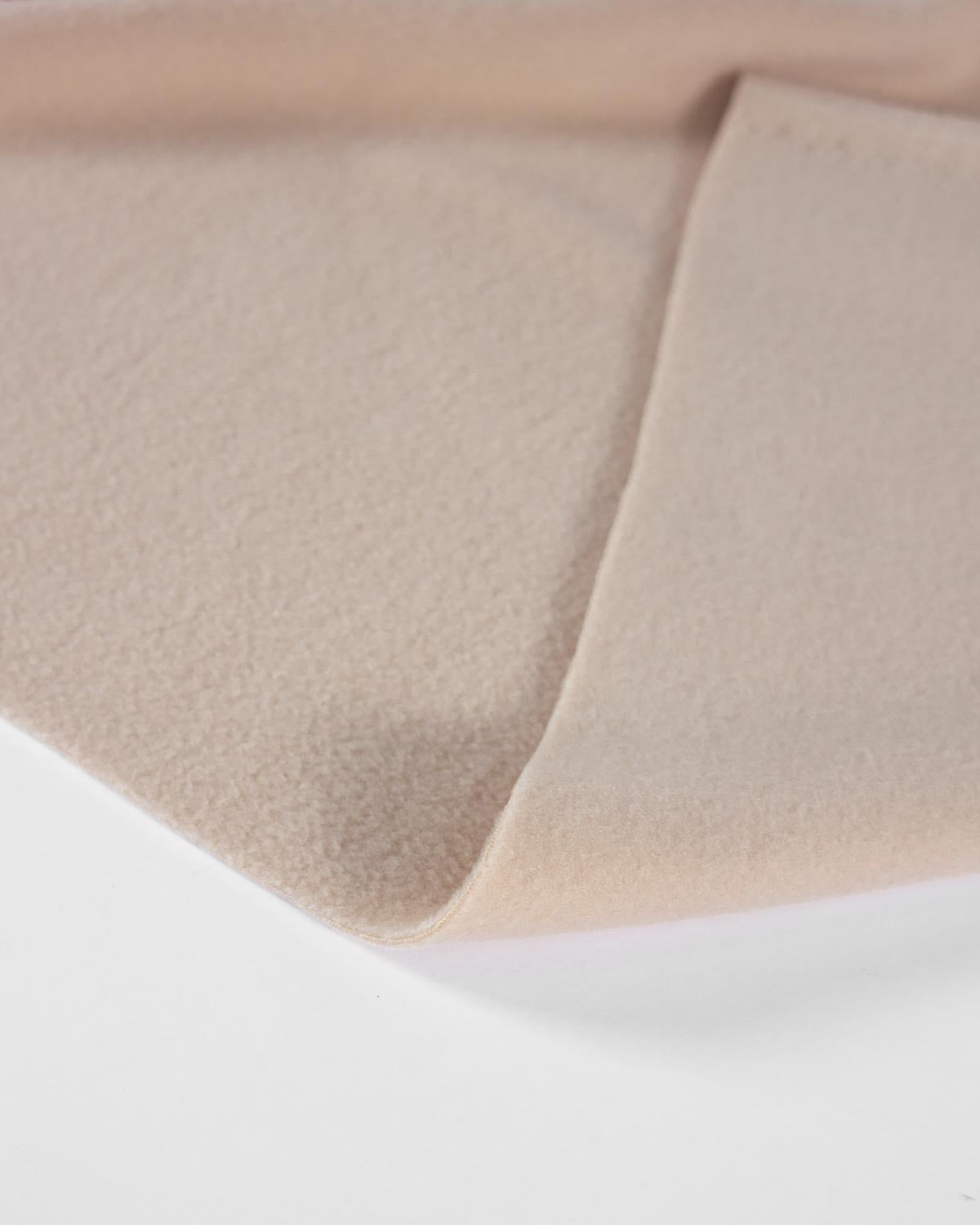 A close-up of a soft, light beige fleece fabric with a folded corner, showing its fine texture against a clean white background.