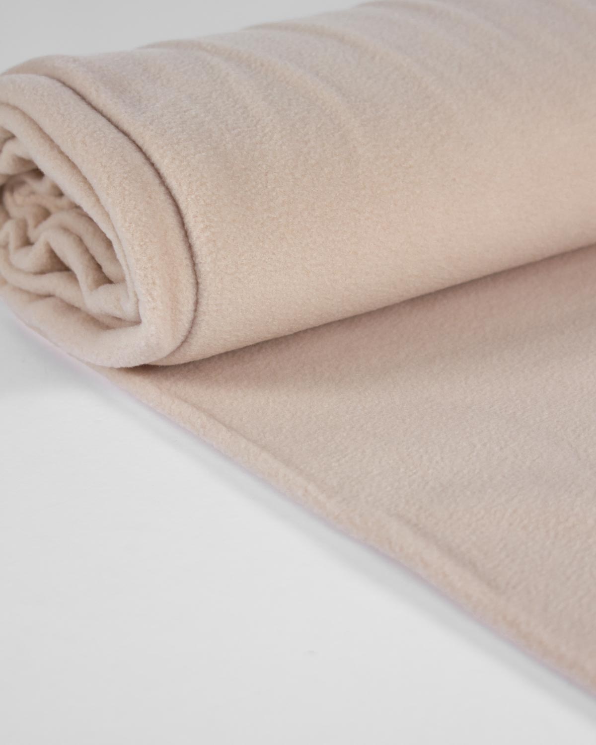 A close-up of a soft, rolled beige fleece fabric roll on a clean white surface.