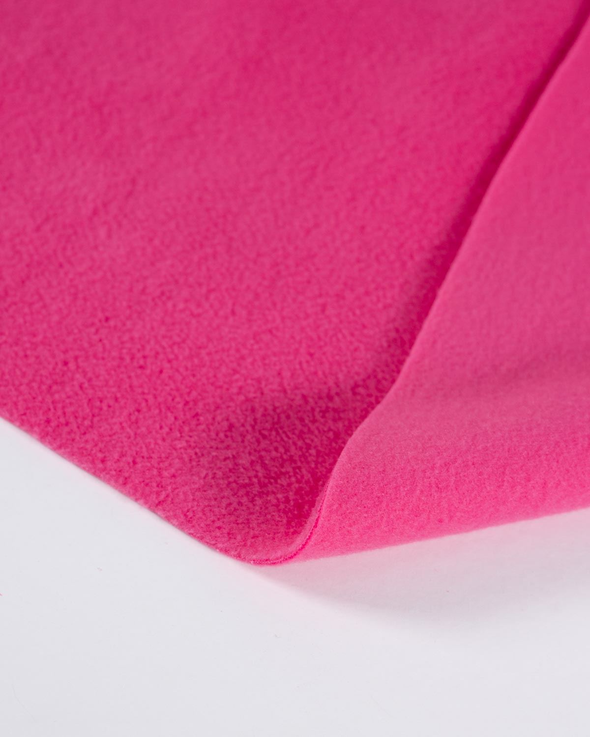 A close-up of bright pink fleece fabric with a soft, textured surface, folded over on a white background.